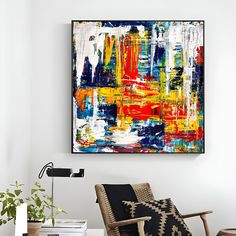 an abstract painting hangs on the wall next to a chair and table with a plant