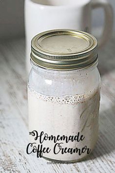 a white coffee mug sitting on top of a wooden table next to a mason jar