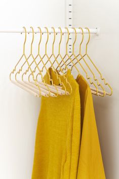 three yellow shirts hanging on a clothes rack next to a white coat hanger with two pairs of yellow sweaters