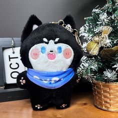 a small stuffed animal with a blue scarf around it's neck sitting next to a christmas tree