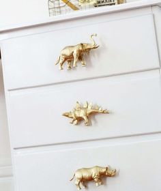 three gold rhino figurines sitting on top of a white chest of drawers in a child's room