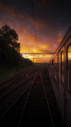 the sun is setting over train tracks with trees on each side and power lines in the distance