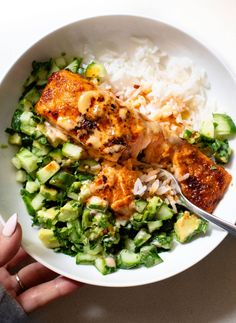 someone is holding a fork over a bowl of food that includes rice, broccoli and chicken