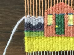 a close up of a weaving machine with yarn on it and a small house in the background