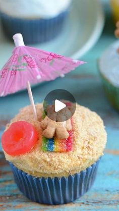 a cupcake with a teddy bear on top and an umbrella in the middle is sitting next to other cupcakes