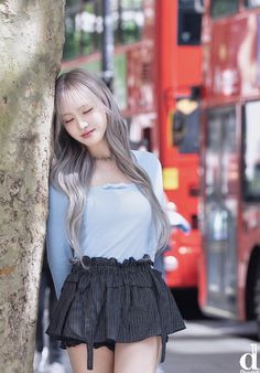 a woman standing next to a tree in front of a bus