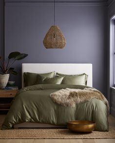 a bed with green sheets and pillows next to a potted plant in front of a window