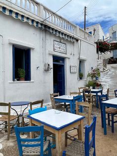 several tables and chairs are outside in front of a white building with blue shutters