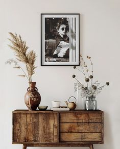 a wooden dresser topped with vases and flowers next to a wall mounted photo on the wall