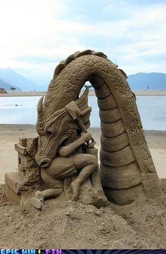 a sand sculpture of a dragon and a woman on the beach