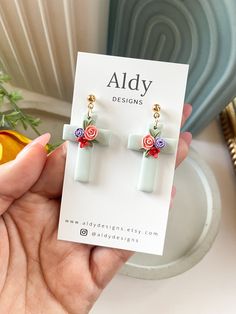 a person holding up a pair of earrings in front of a white plate with flowers on it