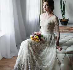 a woman in a white dress sitting on a couch holding a flower bouquet and looking off into the distance