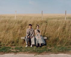 two people sitting on a bench in a field