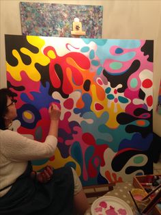 a woman sitting in front of a colorful painting