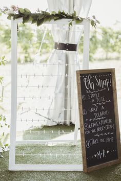 a chalkboard sign sitting in front of a white arch with greenery on it