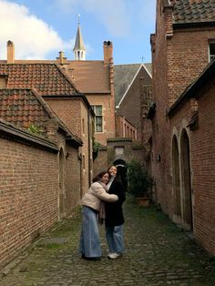 two women are standing in an alleyway with brick buildings on either side and one woman is hugging the other