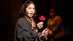 a woman holding a red flower in her right hand while standing next to other people