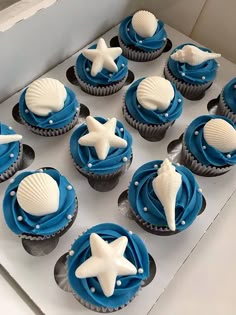 blue and white cupcakes with seashells on them are in a box