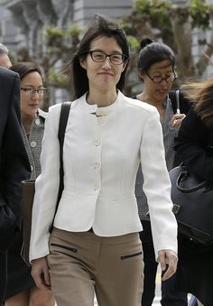 a woman wearing glasses and a white jacket walking down the street with other people behind her