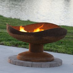 a fire pit sitting on top of a cement slab next to a body of water