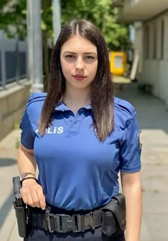 a woman police officer is standing on the street with her hand in her pocket and looking at the camera