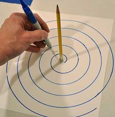 a person is holding a pencil and drawing on paper with blue circles in the middle