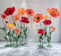 there are many red and orange flowers in vases on the floor next to each other