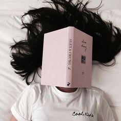 a woman laying on top of a bed with a pink box on her head over her head