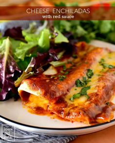 cheese enchiladas with red sauce on a white plate next to a salad