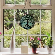 a window sill filled with potted plants next to a tree shaped hanging decoration