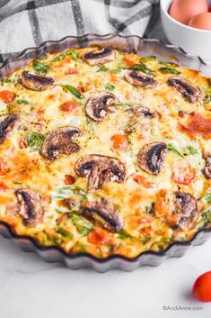 a quiche with cheese, mushrooms and tomatoes in a pie pan next to eggs