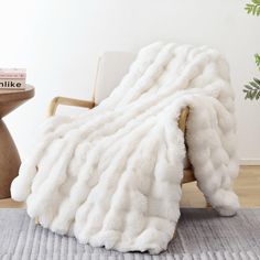 a white blanket sitting on top of a wooden chair next to a potted plant