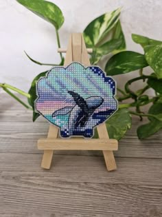 a small wooden easel holding a cross - stitch picture of an orca whale