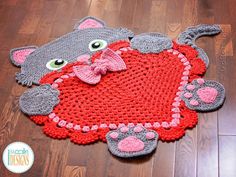 a crocheted rug with a cat holding a heart on it's back