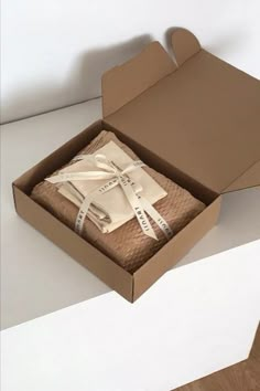 an open cardboard box with two pieces of paper wrapped in white ribbon on the inside