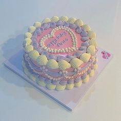 a pink and white birthday cake sitting on top of a table next to a card