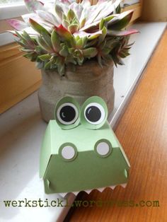 a potted plant sitting on top of a window sill next to a paper frog