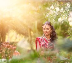 a woman wearing a red and white sari standing in front of some trees with her hands on her hips