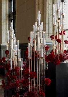 red and white flowers are in vases on the floor next to tall metal poles