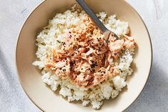 a bowl filled with rice and meat on top of a white table cloth next to a fork