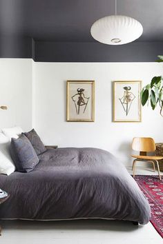 a bed sitting in a bedroom next to two pictures on the wall and a rug