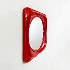 a red mirror mounted to the side of a wall next to a white wall and floor