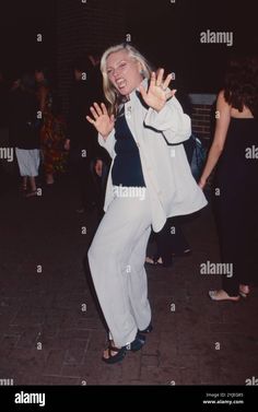 a woman in white pants and black top dancing on the street at night time - stock image