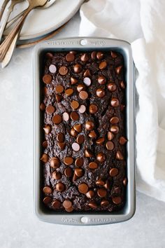 a chocolate brownie in a pan with spoons on the side and napkin next to it