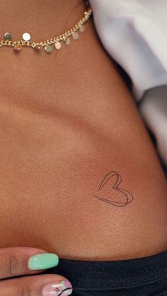 a woman's stomach with a small heart tattoo on her left side ribcage