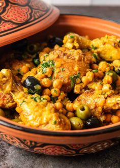 an orange bowl filled with chickpeas and olives on top of a table