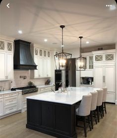 a large kitchen with white cabinets and black island in the center is lit by pendant lights