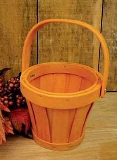 an orange basket sitting on top of a wooden floor next to a bunch of leaves