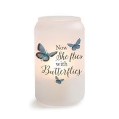 a white candle with blue butterflies on it and the words now she flies with butterflies