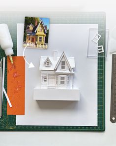 a paper model of a house on top of a cutting board with scissors and glue